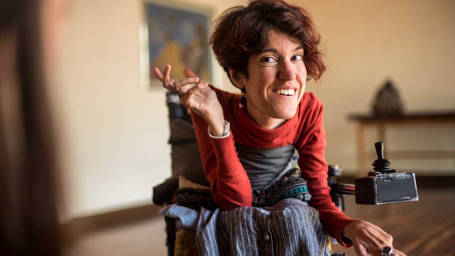 Woman sitting in a wheelchair, smiling at something off camera, gesturing.